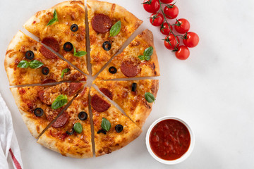 Cut into slices delicious fresh pizza with  pepperoni on a white background. Top view. Pizza on the white table.