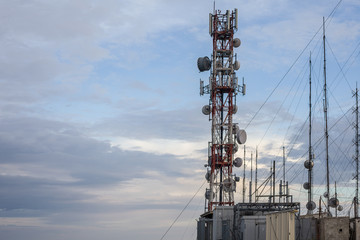 An network tower standing tall near the cliff besides a sandy beach. Dozens of wire connected to each transmission to give supply of reception signal in that rural area.