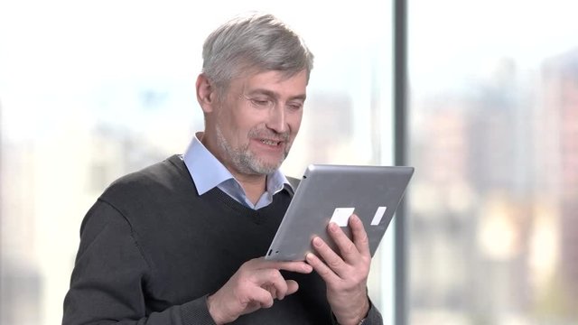 Smiling mature man using digital tablet. Handsome senior man talking via internet using computer tablet on blurred background.