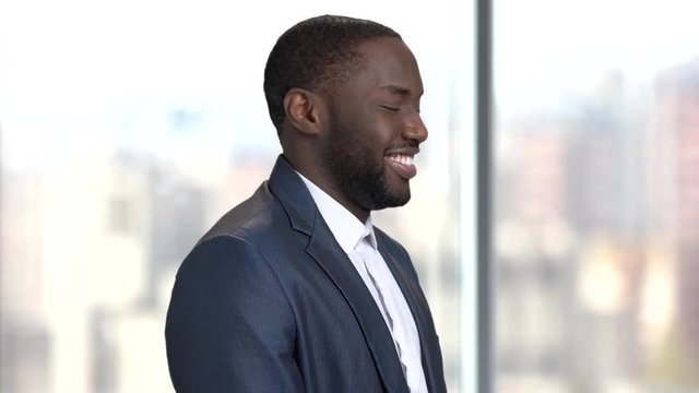 Afro-american man winks with eye. Flirtatious african-american businessman on blurred background. Handsome dark-skinned macho-man.