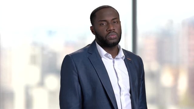 Serious businessman adjusting his shirt. Dark-skinned entrepreneur on blurred background.