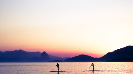 Two people practice stand-up paddle at dusk surrounded by paradisiacal coasts in Niteroi, RJ...