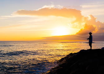 Fototapeta premium Man fishing by the sea at sunset.