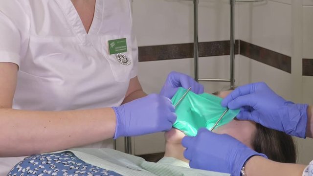 Woman at dentist clinic gets dental treatment to fill a cavity in a tooth. Dental restoration and composite material polymerization with UV light and laser. Installation of dental dam.