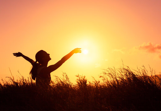 Young woman in a beautiful nature sunset setting raising her arms up in the air. Happiness freedom and joy concept. 