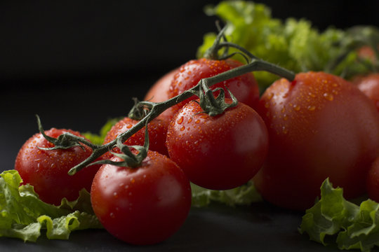 Fresh tomatoes with greens on a black background.