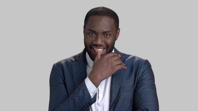 Handsome macho-man on grey background. Portrait of afro-american businessman is winking with eye and smiling.