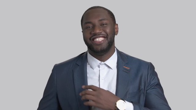 Black macho-man on grey background. Smiling afro-american macho adjusting his suit and looking at camera.