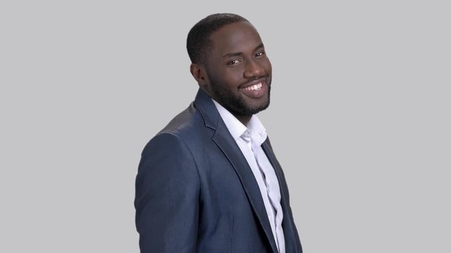 Joyful macho-man on grey background. Smiling afro-american businessman is adjusting his shirt. Successful black businessman.