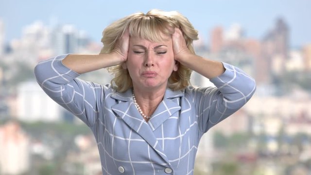 Stressed woman pulling out her hair. Frustrated mature blonde on blurred background. Stress and frustration concept.