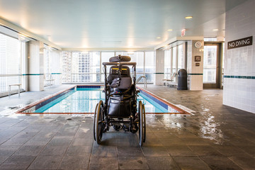Wheelchair at the edge of a swimming pool with no diving sign - 209508517
