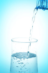 Pouring water from bottle into glass on white background.