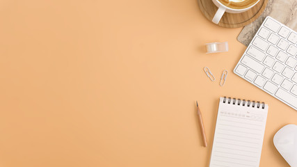 Flat lay, top view office table desk. Workspace with blank note book, keyboard, office supplies and coffee cup on light brown background.