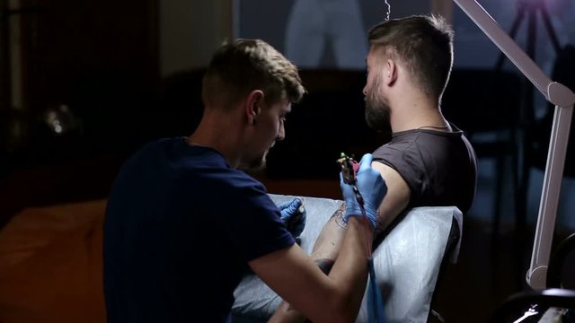 A brutal man makes himself a tattoo in a tattoo parlor. The process of creating a tattoo on the man's arm.