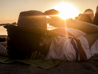 close up silhouette of man lying on the sand on the beach with hat on face