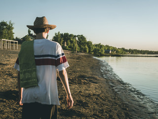 back view of young man in summer hat walking on the beach during golden hour