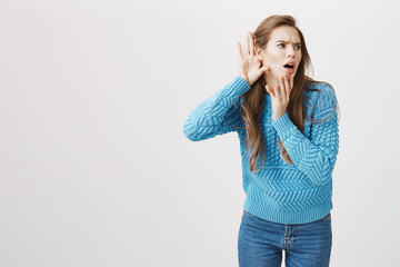Portrait of european adult woman expressing interest while bending to camera holding hands near ear...
