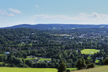 Obraz premium View from hill suburbs of London, United Kingdom. Green trees, small houses, meadows and lawns. Blue sky with clouds.