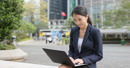 Adult student works on laptop, outside, during a workbreak; dressed professionally