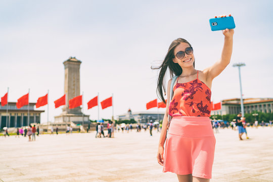Asian woman taking selfie photo with phone in Beijing, China. Asia travel. Tourist girl sightseeing famous sight holding mobile smartphone visiting Tiananmen Square. Summer vacation.