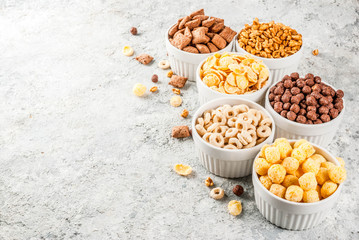 Set of various breakfast cereal corn flakes, puffs, pops, grey stone table copy space