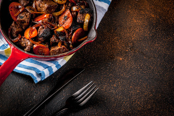 Roasted or grilled beef liver with onion and carrot in portioned frying pan, dark rusty  table copy space top view
