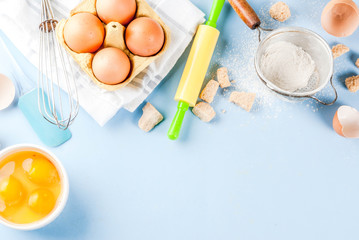 Ingredients and utensils for cooking baking egg, flour, sugar, whisk, rolling pin, on blue background, top view copy space