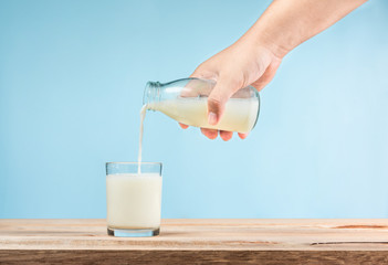Pouring milk into a glass on wooden table on blue background