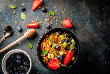 Healthy breakfast with muesli or granola with nuts and fresh berries and fruits - strawberry, blueberry, kiwi, on dark blue table, copy space top view