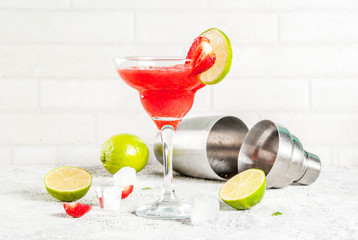 Cold strawberry margarita cocktail with ice, lime and fresh berries in margarita glass, light grey background copy space