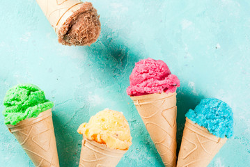 Selection of various bright multicolored ice-cream in ice cream cones - chocolate vanilla blueberry strawberry pistachio orange, on light blue sunny background, copy space top view