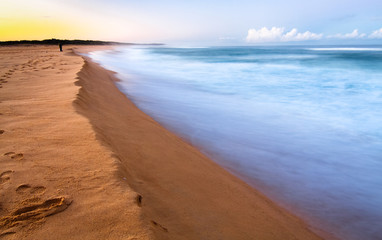 Long exposure of waves crashing on an orange sandy beach at sunset. Tuross Head, New South Wales, Australia.