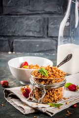 Homemade granola from mix of cereals (barley, oat, rye, bran) with with strawberry, mint leaves and fresh organic milk on dark blue concrete background