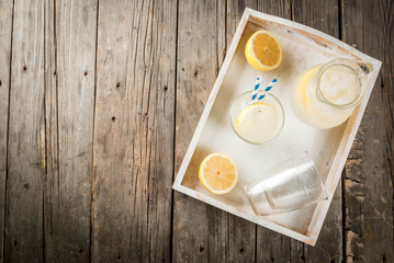 Classic sour and sweet homemade lemonade drink, summer cold iced beverage, rustic wooden background copy space in white tray above