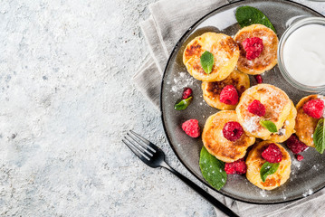 Healthy summer breakfast, cheese pancakes with raspberry, powdered sugar and mint, grey concrete background copy space