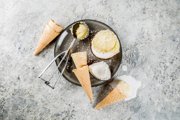 Summer healthy dessert, organic vegan coconut ice cream served in halves of coconut and ice cream cones, gray concrete background