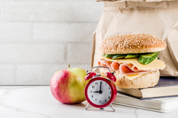 Healthy school food concept, paper bag with lunch, apple, sandwich, books and alarm clock on white...