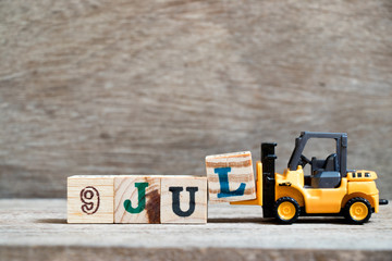 Toy forklift hold block l to complete word 9 jul on wood background (Concept for calendar date in month July)