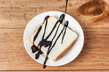 chocolate syrup on white sliced bread on dish, wooden background