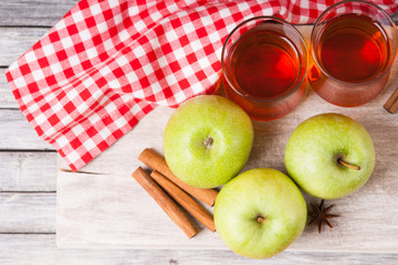 Apple juice in glasses, spices and apples on wooden cutting table 
