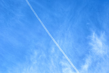 Smoke from the jet engine show diagonal with the blue sky in the background.