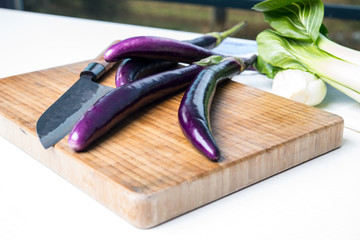 japanese eggplant on wooden board with knife and pak choi salad