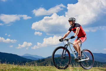 Fototapeta na wymiar Athletic sportsman bicyclist in sportswear and helmet riding cross country bike in the Carpathian mountains, summer blue sky with clouds on background. Active lifestyle and extreme sport concept.