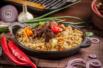 The concept of eastern, Uzbek cuisine. Pilaf, plov in a black cast-iron frying pan on a wooden...