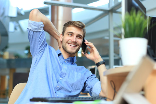 Smiling businessman sitting and using mobile phone in office.