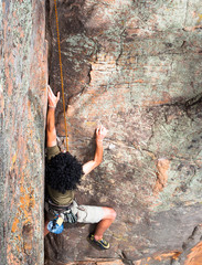 A climber with large black afro climbs a rock wall at the Black Ians climbing area in Victoria, Australia.