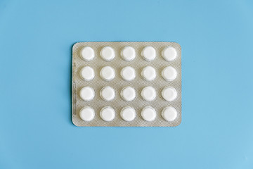 White pills and blister pack on blue pastel colored background. Pharmaceutical industry minimal...