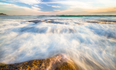 Long exposure of ocean waves flowing over rocky tidepools at sunset on Johanna Beach in the Great...