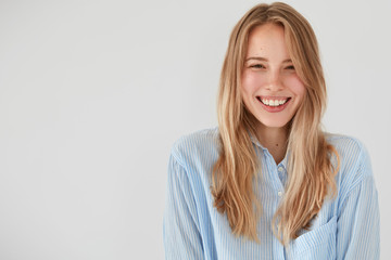 Joyful pretty young woman giggles positively at camera, dressed in casual shirt, shows beauty,...
