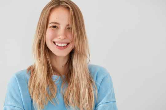 Studio shot of happy Caucasian female has broad smile, shows white teeth, being in high spirit after celebrating friend`s birthday, enjoys recreation time in merry company, isolated over white wall